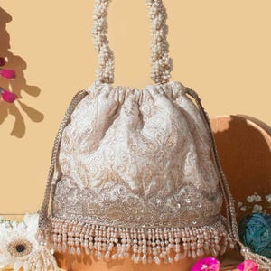 May include: A white and gold embroidered drawstring bag with a pearl handle and tassel. The bag has a beaded fringe and is decorated with sequins.