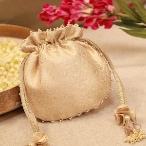 Könnte beinhalten: Eine goldene Brokat-Kordeltasche mit Perlenbesatz und Quastenakzenten. Die Tasche ist geschlossen und hat eine runde Form.