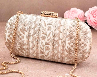 May include: Ivory clutch with gold floral embroidery and a gold chain strap. The rectangular bag features a gold clasp and is decorated with intricate patterns. A stylish accessory for special occasions.