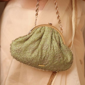 Puede incluir: Un bolso de mano verde salvia con intrincados bordados florales y un cierre dorado. El bolso presenta una correa de cadena dorada y una tela delicada y texturizada. El diseño es elegante y adecuado para ocasiones especiales.