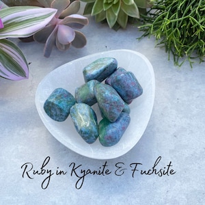May include: A small bowl filled with tumbled stones of ruby in kyanite and fuchsite. The stones are a mix of green and blue with red flecks.