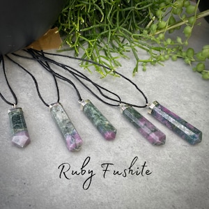 May include: Six green and pink ruby fuchsite pendants on black cords. The pendants are all faceted and have a silver bail. The text "Ruby Fuschite" is written below the pendants.