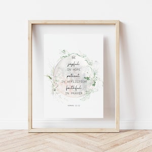 May include: A framed print featuring a watercolour design of a moon with green foliage surrounding it. The text reads "Be joyful in hope, patient in affliction, faithful in prayer, Romans 12:12".
