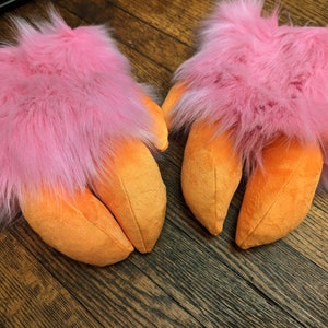 May include: A pair of pink and orange plush hand puppets with three claws each. The puppets are made of soft, fluffy fabric and have a realistic claw design.