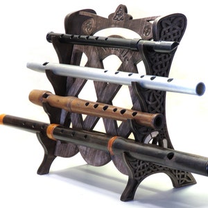 Puede incluir: Soporte de madera con un intrincado diseño de nudos celtas, que sostiene cinco flautas diferentes de madera y metal.
