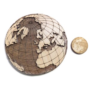 May include: A wooden globe with a detailed map of the world, featuring a grid pattern and a smaller wooden disc.