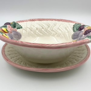 May include: A white ceramic bowl with a pink rim and a woven basket design. The bowl has a matching plate with a pink rim and a woven basket design. The bowl and plate are decorated with painted fruit and vegetables.