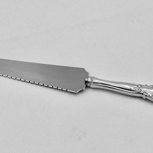 May include: A silver cake server with a serrated edge and an ornate handle.