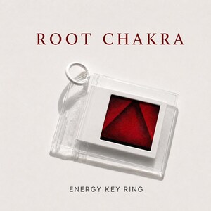 May include: A white key ring with a clear plastic case holding a white frame with a red triangle design. The text "ROOT CHAKRA" is above the key ring, and "ENERGY KEY RING" is below.