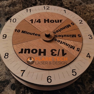 Peut inclure: Un cadran d'horloge en bois avec un cadran rotatif. Le cadran est divis&eacute; en sections qui montrent 1/4 d'heure, 1/3 d'heure, 10 minutes et 5 minutes. Le cadran de l'horloge est marqu&eacute; des chiffres 1 &agrave; 12. Le texte "FLARE TECH LASER & DESIGN" est imprim&eacute; sur le cadran de l'horloge.