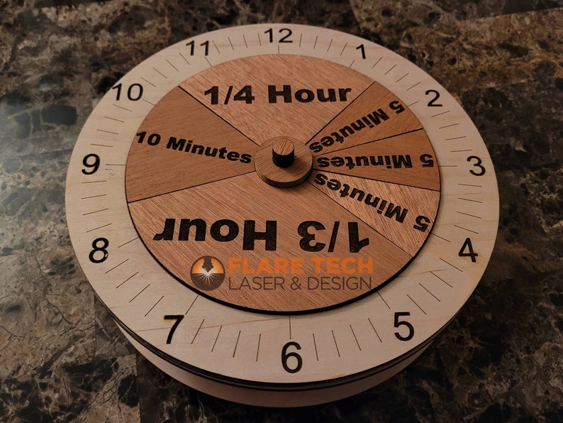 Peut inclure: Un cadran d'horloge en bois avec un cadran rotatif. Le cadran est divis&eacute; en sections qui montrent 1/4 d'heure, 1/3 d'heure, 10 minutes et 5 minutes. Le cadran de l'horloge est marqu&eacute; des chiffres 1 &agrave; 12. Le texte "FLARE TECH LASER & DESIGN" est imprim&eacute; sur le cadran de l'horloge.