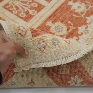 May include: A close-up of a beige and orange rug with a floral pattern. The rug has a fringe border and is folded in half.