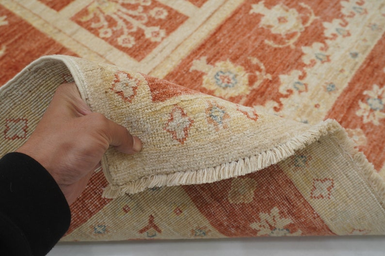 May include: A close-up of a beige and orange rug with a floral pattern. The rug has a fringe border and is folded in half.