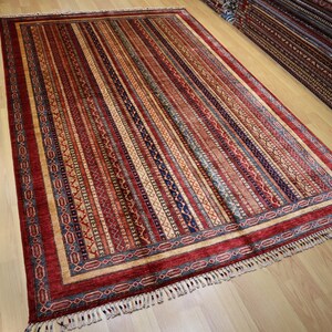May include: A colorful rug with a striped pattern and a border of intricate designs. The rug has a fringe on all sides.