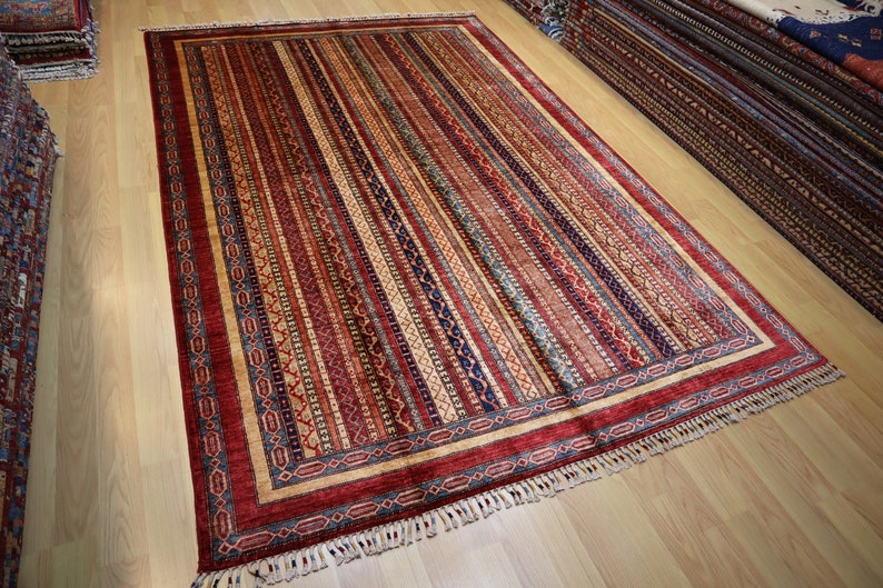 May include: A colorful rug with a striped pattern and a border of intricate designs. The rug has a fringe on all sides.