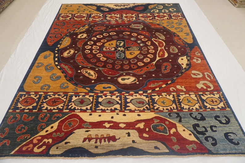 Op de afbeelding: Een kleurrijk tapijt met een centraal medaillonontwerp met ingewikkelde patronen en geometrische vormen. Het tapijt heeft een donkerblauwe achtergrond met accenten in rood, geel en beige.