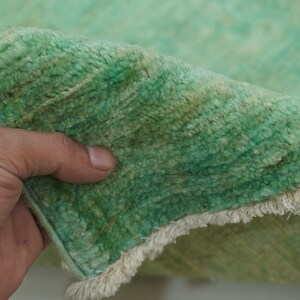 May include: Close-up of a green rug with a white fringe. The rug is soft and fluffy, and the fringe is made of a thin, white yarn.