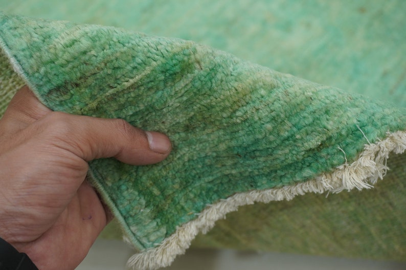 May include: Close-up of a green rug with a white fringe. The rug is soft and fluffy, and the fringe is made of a thin, white yarn.
