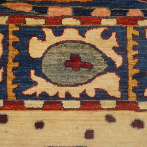 Op de afbeelding: Close-up van een tapijt met een blauwe achtergrond en een cr&egrave;mekleurig patroon. Het patroon bevat gestileerde bloemmotieven en een centraal medaillon met een rood kruis.