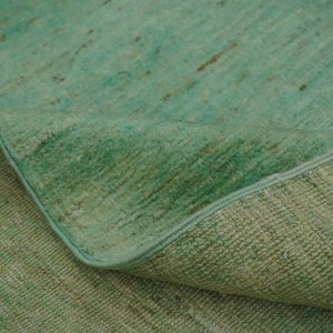 May include: A close-up of a green rug with a textured surface. The rug is folded in half, showing the underside of the fabric.