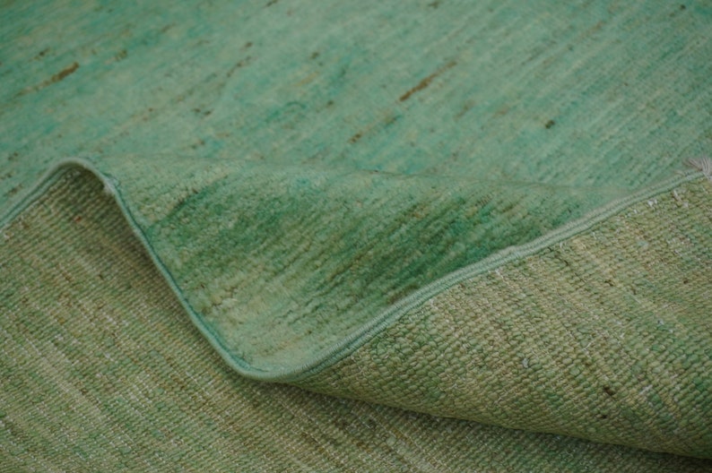 May include: A close-up of a green rug with a textured surface. The rug is folded in half, showing the underside of the fabric.