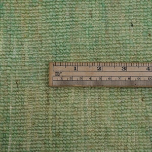 May include: Close-up of a green woven rug with a white fringe. A ruler is placed on the rug to show the texture and weave. The ruler measures 5 inches.