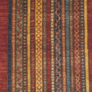 Może przedstawiać: Prostokątny dywan z powtarzającym się wzorem pionowych pask&oacute;w. Dywan ma paski w odcieniach czerwieni, niebieskiego, ż&oacute;łtego i zielonego. Wz&oacute;r zawiera motywy geometryczne i kwiatowe, tworząc teksturowany wygląd. Dywan jest prawdopodobnie wykonany z tkanego materiału.