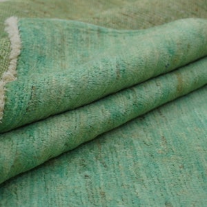 May include: A green rug with a fringed edge. The rug is folded in half, showing the texture of the fabric.