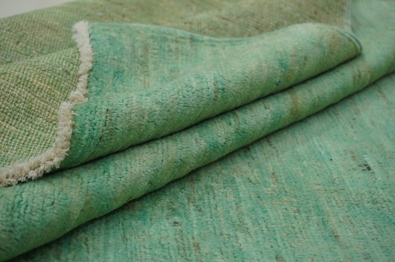 May include: A green rug with a fringed edge. The rug is folded in half, showing the texture of the fabric.