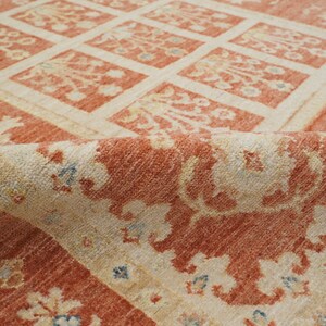 May include: A close-up of a red and cream colored rug with a floral pattern. The rug is folded in half, showing the intricate details of the design.