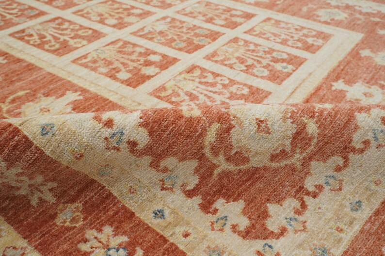 May include: A close-up of a red and cream colored rug with a floral pattern. The rug is folded in half, showing the intricate details of the design.
