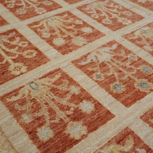 May include: A close-up of a beige and orange patterned rug with a repeating floral design. The rug has a subtle sheen and a soft texture.