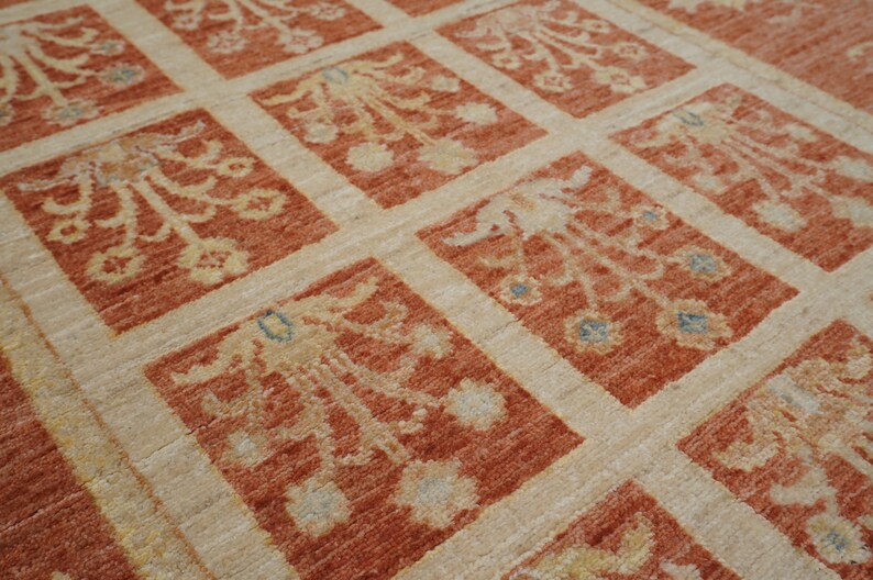 May include: A close-up of a beige and orange patterned rug with a repeating floral design. The rug has a subtle sheen and a soft texture.