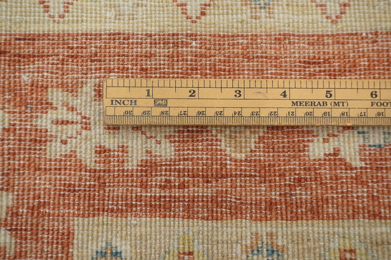 May include: Close-up of a wooden ruler measuring 6 inches, with markings in inches and centimeters. The ruler is placed on top of a red and white patterned rug.