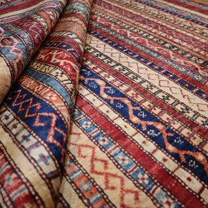 May include: A traditional rug with a colorful striped pattern in shades of red, blue, and cream. The rug has a geometric design with intricate details.
