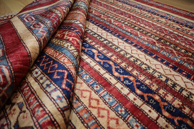 May include: A traditional rug with a colorful striped pattern in shades of red, blue, and cream. The rug has a geometric design with intricate details.