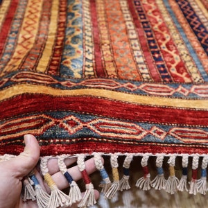May include: A colorful hand-woven rug with intricate patterns in shades of red, blue, yellow, and beige. The rug has a fringe border and is folded in half.