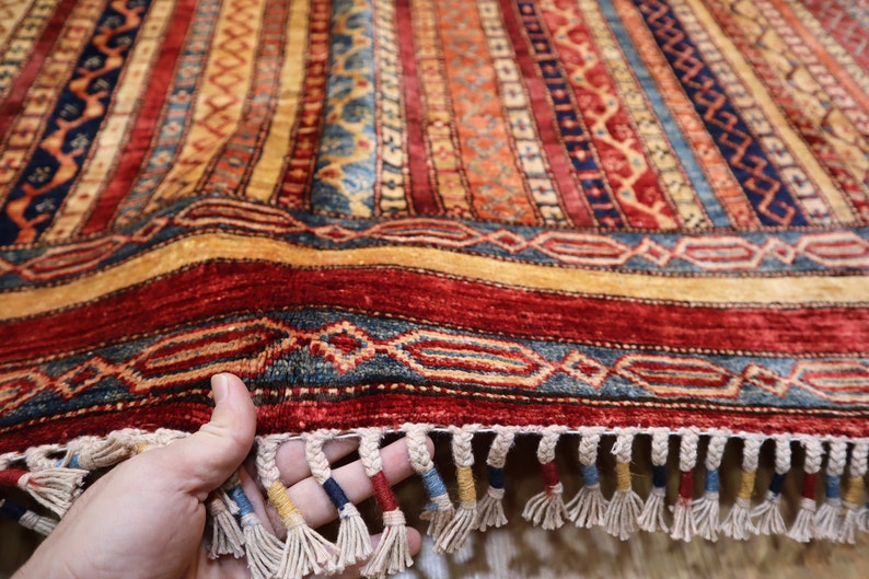 May include: A colorful hand-woven rug with intricate patterns in shades of red, blue, yellow, and beige. The rug has a fringe border and is folded in half.