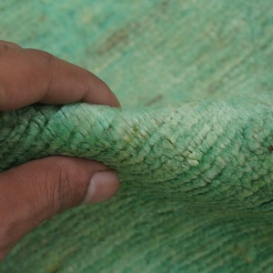 May include: Close-up of a soft, green rug with a textured surface. The rug is made of a woven material and has a subtle sheen.