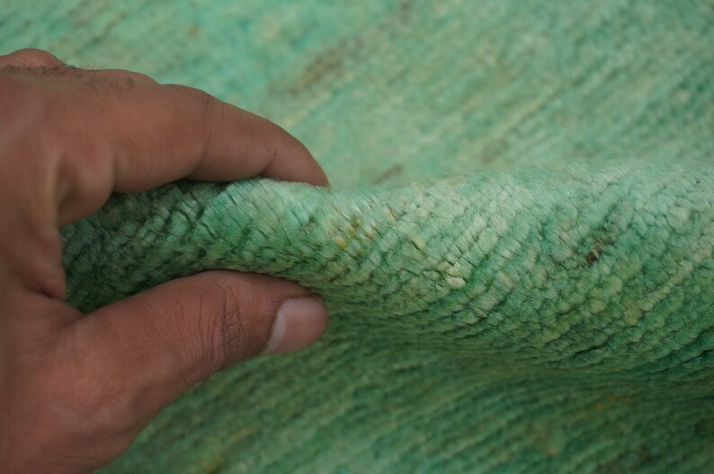May include: Close-up of a soft, green rug with a textured surface. The rug is made of a woven material and has a subtle sheen.