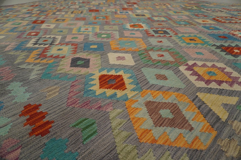 May include: A colorful rug with a geometric pattern in shades of blue, green, orange, red, and pink. The rug has a gray background and a diamond-shaped design.