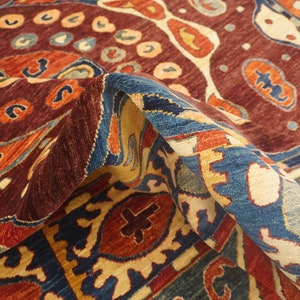 Op de afbeelding: Een kleurrijk tapijt met ingewikkelde patronen in tinten rood, blauw, oranje en cr&egrave;me. Het tapijt heeft een traditioneel ontwerp met een centraal medaillon en herhalende motieven.