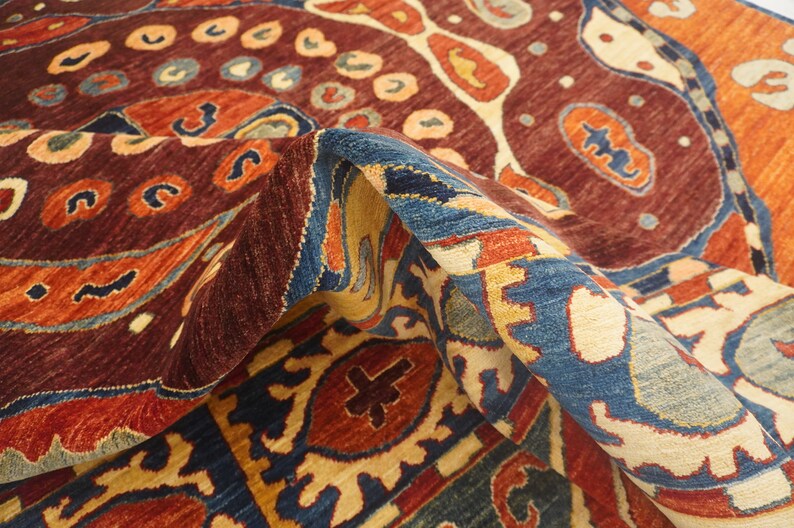 Op de afbeelding: Een kleurrijk tapijt met ingewikkelde patronen in tinten rood, blauw, oranje en cr&egrave;me. Het tapijt heeft een traditioneel ontwerp met een centraal medaillon en herhalende motieven.