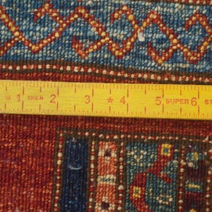 Może przedstawiać: Zbliżenie fragmentu dywanu z ż&oacute;łtą linijką. Dywan ma czerwony, niebieski i złoty wz&oacute;r. Linijka mierzy do 20 cm.