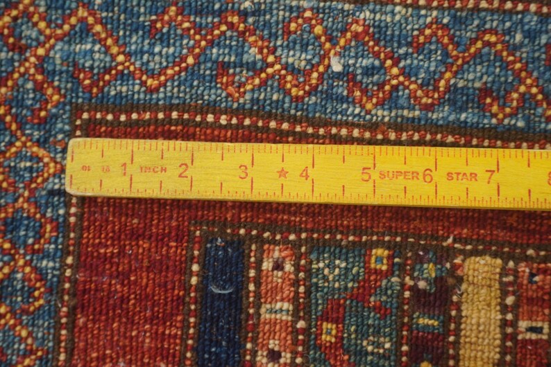 Może przedstawiać: Zbliżenie fragmentu dywanu z ż&oacute;łtą linijką. Dywan ma czerwony, niebieski i złoty wz&oacute;r. Linijka mierzy do 20 cm.