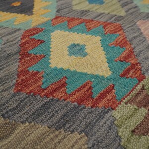 May include: Close-up of a colorful woven rug with a geometric pattern. The rug features shades of blue, red, yellow, and green.
