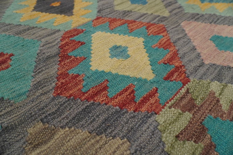 May include: Close-up of a colorful woven rug with a geometric pattern. The rug features shades of blue, red, yellow, and green.