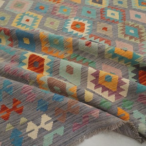 May include: A gray rug with a geometric pattern in shades of orange, blue, green, and pink. The rug has a fringed edge.