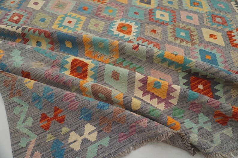 May include: A gray rug with a geometric pattern in shades of orange, blue, green, and pink. The rug has a fringed edge.