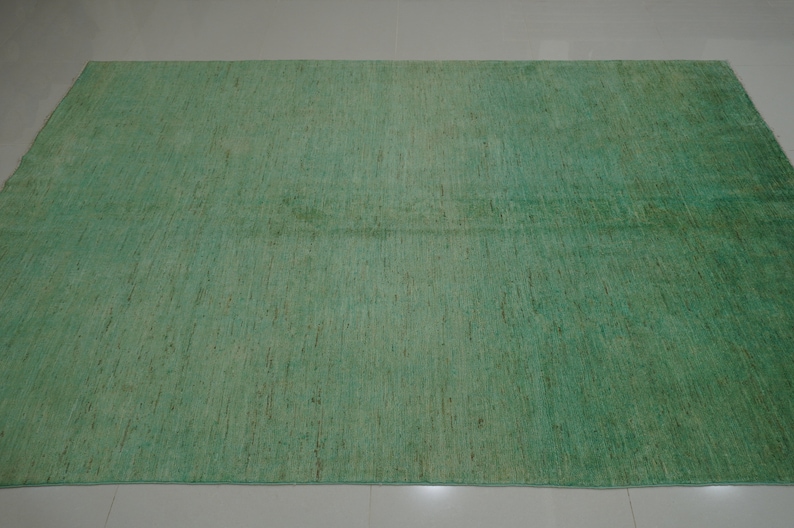 May include: A green area rug with a subtle, textured pattern. The rug has a slightly faded appearance, giving it a vintage look.